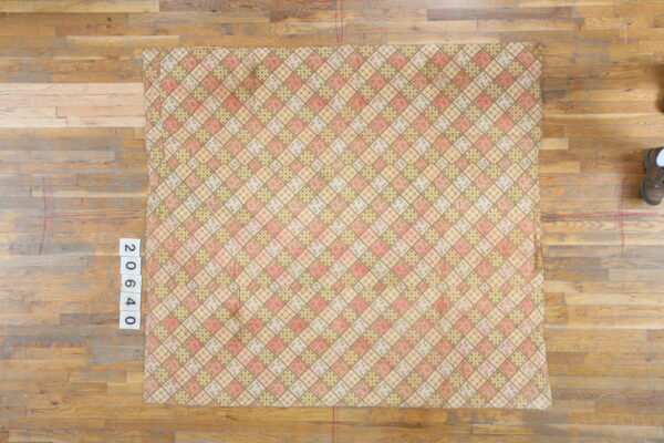 Pink, beige, and green argyle rug with assorted small patterns resting on a light wood floor.