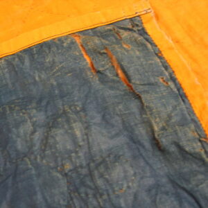 Distressed blue textile with visible tears meets a plain golden-orange fabric border with black stitching.