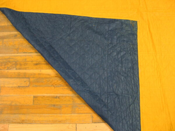 A bright yellow rug corner is folded, revealing a quilted dark blue backing on hardwood flooring.