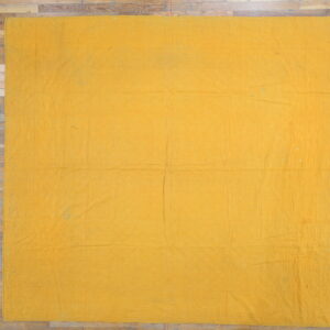 Flat mustard yellow textile with faint geometric stitched patterns laid on wide plank wood flooring.