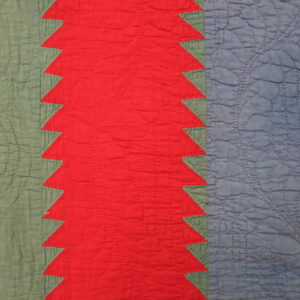 Close-up of a quilted textile featuring red, dusty blue, and sage green vertical stripes with a sawtooth pattern.