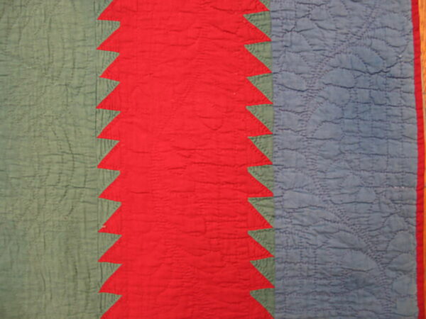 Close-up of a quilted textile featuring red, dusty blue, and sage green vertical stripes with a sawtooth pattern.