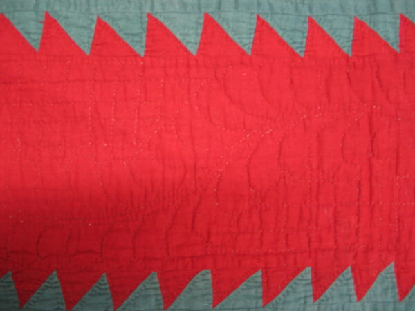 Red and teal low-pile textile featuring a central band with quilted stitching and jagged sawtooth edges.