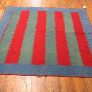 Red and sage sawtooth striped textile with a quilted blue border lying on hardwood planks.