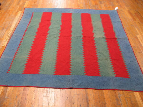 Red and sage sawtooth striped textile with a quilted blue border lying on hardwood planks.
