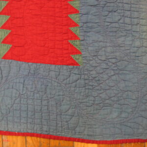 Red sawtooth pattern borders green and heavily quilted blue fabric on wood plank flooring.
