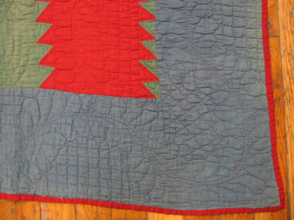 Red sawtooth pattern borders green and heavily quilted blue fabric on wood plank flooring.