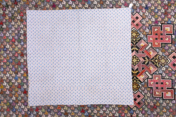 A large square of white fabric with tiny blue flowers overlays a vibrant geometric multicolored rug.