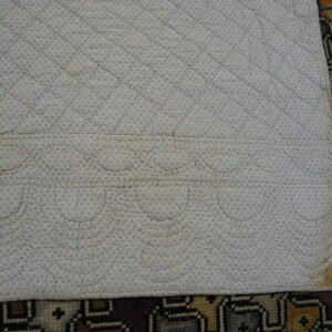 A quilted white and blue dotted fabric pad overlaps a colorful geometric patterned rug below.