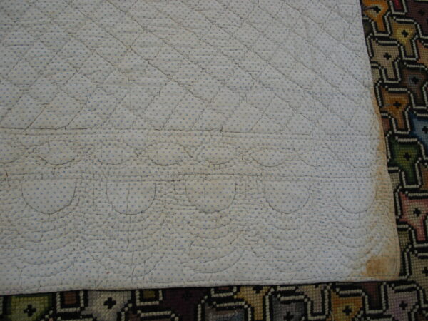 A quilted white and blue dotted fabric pad overlaps a colorful geometric patterned rug below.