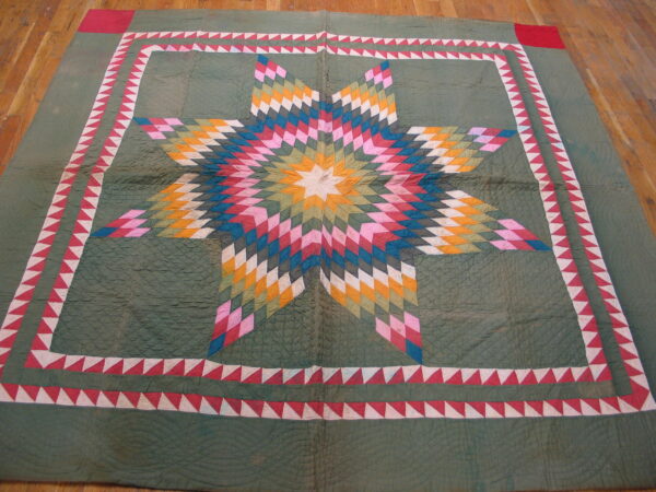 A textured, sage green textile rug lies on a wood floor featuring a bright, multicolor starburst medallion and sawtooth border.