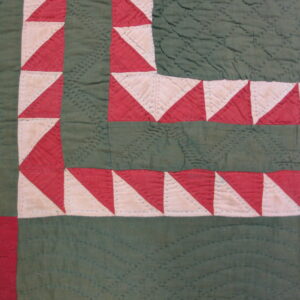 Red and cream triangle border surrounds deep green quilted sections on this textile surface.