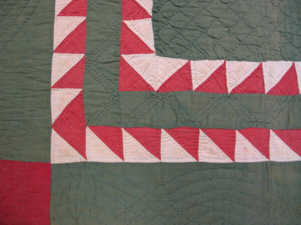 Red and cream triangle border surrounds deep green quilted sections on this textile surface.