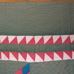 Close-up of green stitched textile showing quilting texture and dual red and cream triangle borders.