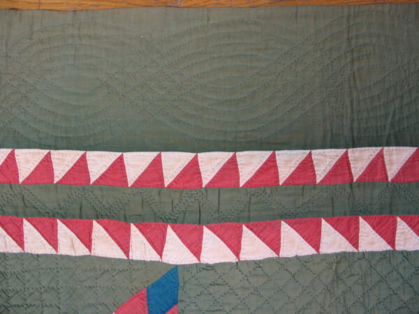 Close-up of green stitched textile showing quilting texture and dual red and cream triangle borders.