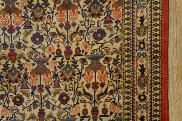 Antique qum iran knotted rug 5 Detailed, short-pile rug in beige, blue, and red featuring intricate floral and geometric patterns bordering light wood.