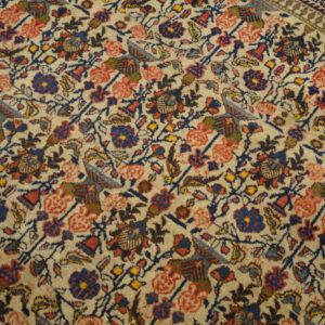 Medium-pile rug detail showing dense floral patterns in navy, coral, and yellow on a cream field.