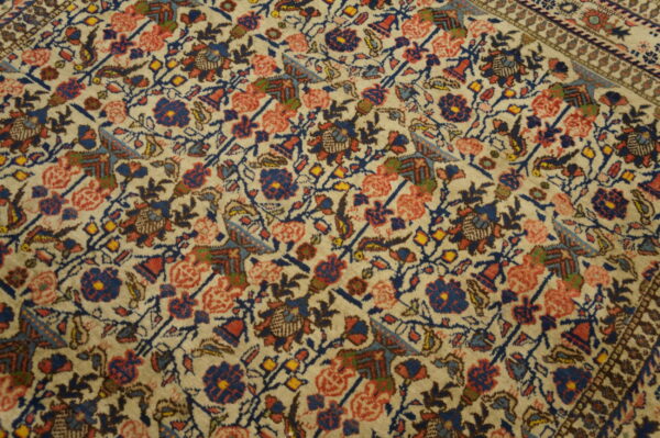 Antique qum iran knotted rug 4 Medium-pile rug detail showing dense floral patterns in navy, coral, and yellow on a cream field.