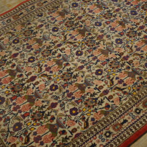 Dense floral and avian motifs in blue, red, and brown cover the cream rug on light wood planks.