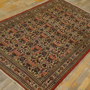 Multicolored low-pile rug with dense floral and bird design and red trim on distressed wood flooring.