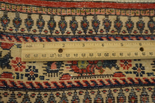 Antique qum iran knotted rug 8 Detailed view of a beige, red, and blue patterned rug with a wooden ruler providing scale reference.