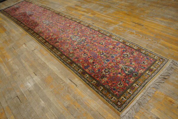 Ornate runner rug in deep rose and multicolor floral designs rests on distressed wood flooring.