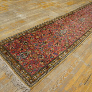 Ornate floral red runner with a gold border and white fringe rests on yellow and gray distressed hardwood.
