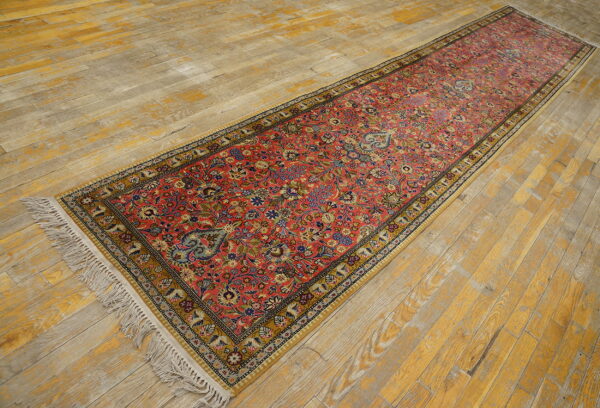 Ornate floral red runner with a gold border and white fringe rests on yellow and gray distressed hardwood.