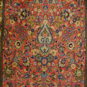 Low-pile rug with a detailed pink field, colorful floral motifs, and wide yellow-gold borders on wood flooring.