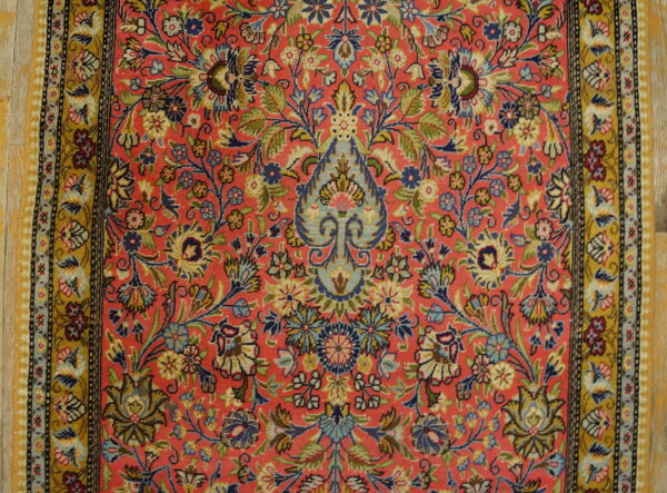 Low-pile rug with a detailed pink field, colorful floral motifs, and wide yellow-gold borders on wood flooring.
