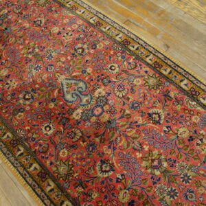 Coral runner rug with dense multi-color floral pattern resting on light, worn wood floors.