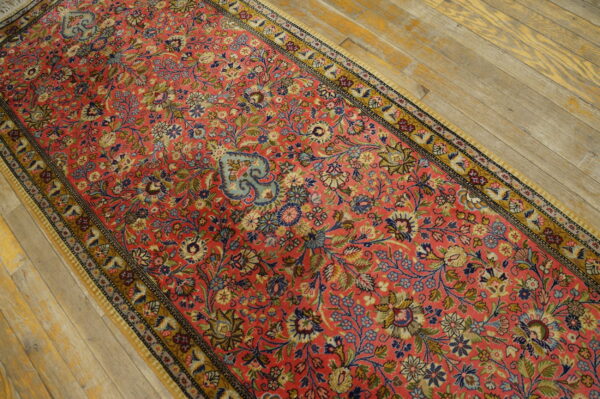 Coral runner rug with dense multi-color floral pattern resting on light, worn wood floors.