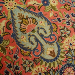 Close-up of a densely patterned rug featuring blue paisley and multicolored florals on a salmon pink pile.