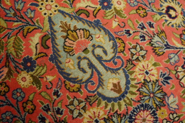 Close-up of a densely patterned rug featuring blue paisley and multicolored florals on a salmon pink pile.