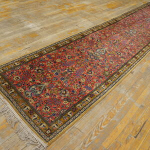 Long red runner rug with dense traditional floral motifs and yellow borders on distressed wood.