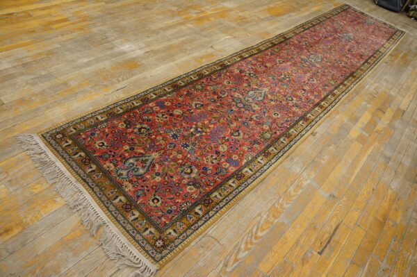 Long red runner rug with dense traditional floral motifs and yellow borders on distressed wood.
