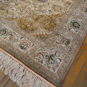 Beige and mustard traditional rug with navy accents and fringe on rustic wood planks.