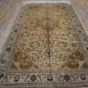 Traditional gold and tan low-pile rug with complex floral design laying on distressed wooden planks.