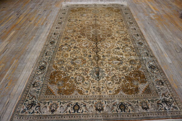 Traditional gold and tan low-pile rug with complex floral design laying on distressed wooden planks.