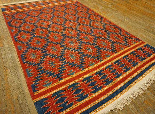 Red and blue flatweave rug with a detailed geometric pattern and striped borders rests on wood floorboards.