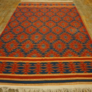 Red and blue flatweave rug featuring geometric zigzag patterns lying on distressed wooden floorboards.