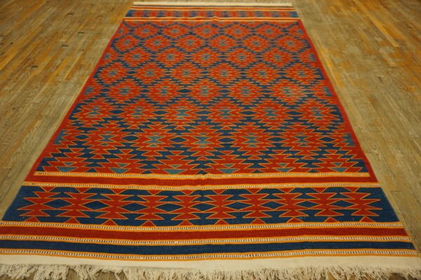 Red and blue flatweave rug featuring geometric zigzag patterns lying on distressed wooden floorboards.