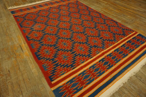Red and blue flatweave rug with a geometric pattern sits on rustic wood plank flooring.