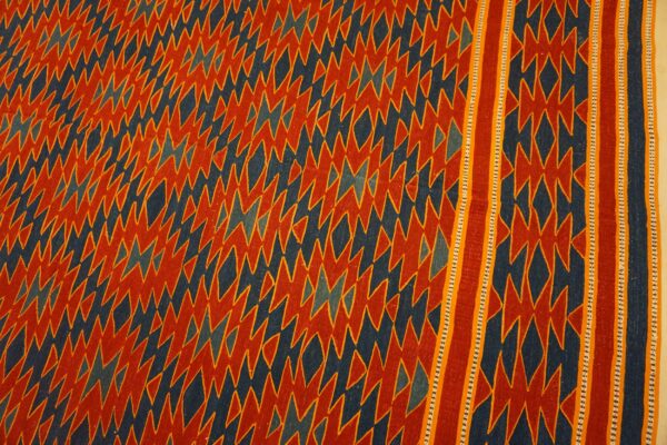 Red-orange and dark blue flatweave rug with densely packed jagged geometric patterns and a distinct striped border.