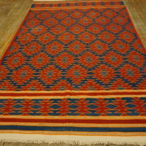 Geometric red and blue flatweave rug with yellow accents and white fringe on a distressed wood floor.