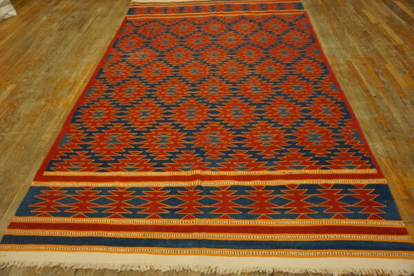 Geometric red and blue flatweave rug with yellow accents and white fringe on a distressed wood floor.