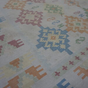 Muted pastel colors form large geometric medallion and hook patterns on a low-pile flat-woven rug.
