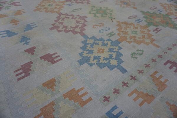 Muted pastel colors form large geometric medallion and hook patterns on a low-pile flat-woven rug.