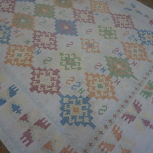 Faded white flatwoven rug with a repeating geometric pattern in pastel colors on rustic wood flooring.