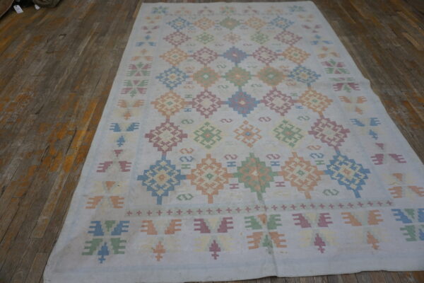 Pale geometric rug with repeating blue, pink, green, and peach patterns displayed on dark wood planks.